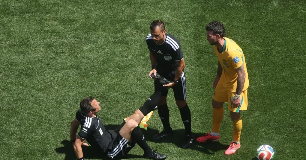 Árbitro Felix Zwayer sentado no gramado recebendo auxílio de jogadores durante EUA x Austrália em Seattle