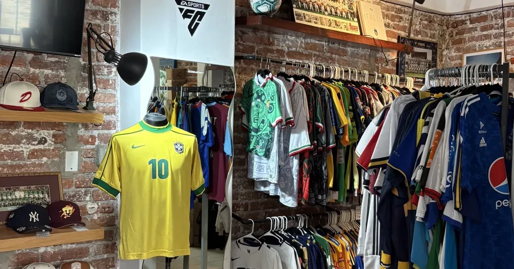 Interior do brechó Es de Época com camisas de futebol penduradas e decoração retrô