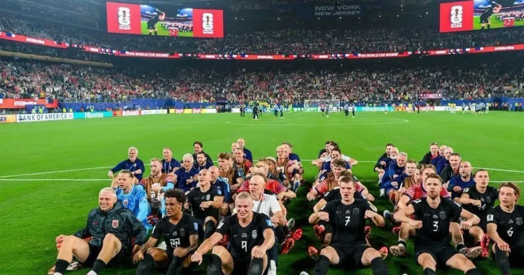 Jogadores da Noruega sentados em fileiras no gramado reproduzindo a remada viking