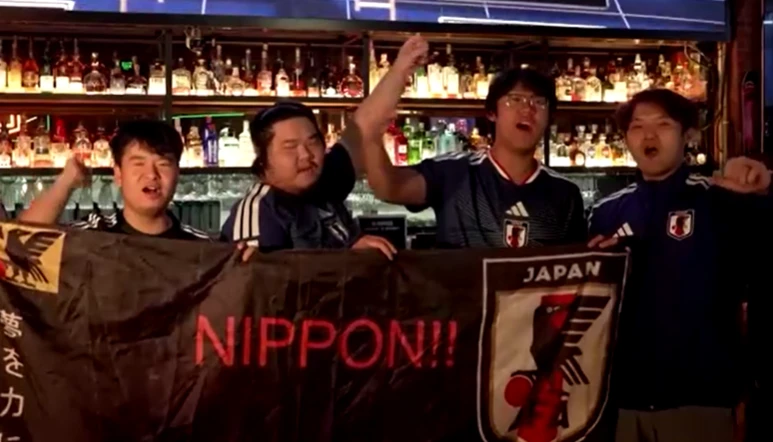 Público em bar de Xangai comemorando gol do Japão, torcedores com camisas azuis