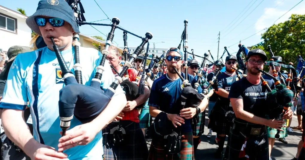 Torcida escocesa Tartan Army marchando por rua de Miami com bandeiras e roupas xadrez