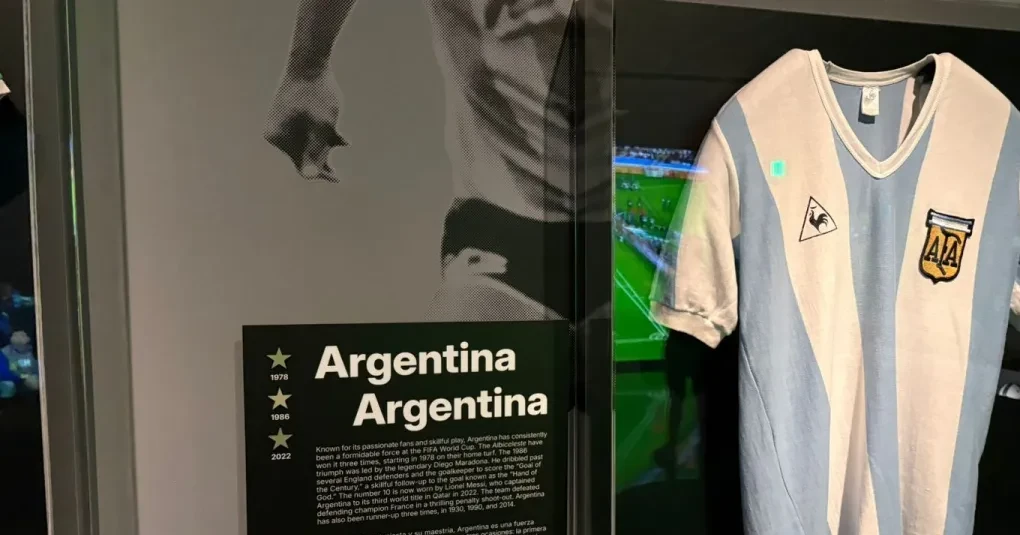 Painel da exposição 'Unidad — The World's Game' na Freedom Tower com camisa exposta e visitantes
