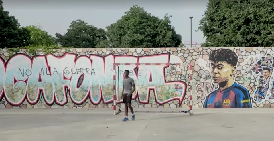 Crianças jogando bola no campo de Rocafonda com mural de Lamine Yamal ao fundo