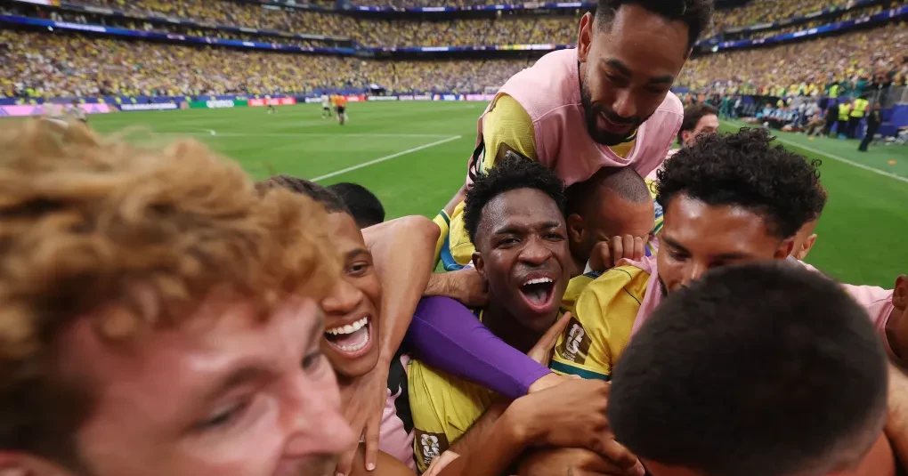 Torcida e jogadores em ação durante partida de Copa do Mundo, com bandeiras nas arquibancadas