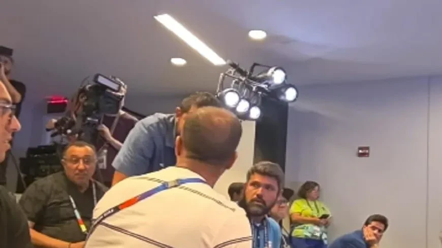 Marcelo Courrege em frente ao microfone durante coletiva, expressão séria