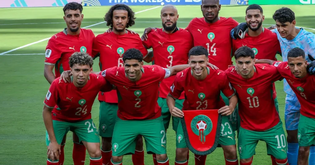 Jogadores da seleção do Marrocos comemorando em campo com bandeira nacional