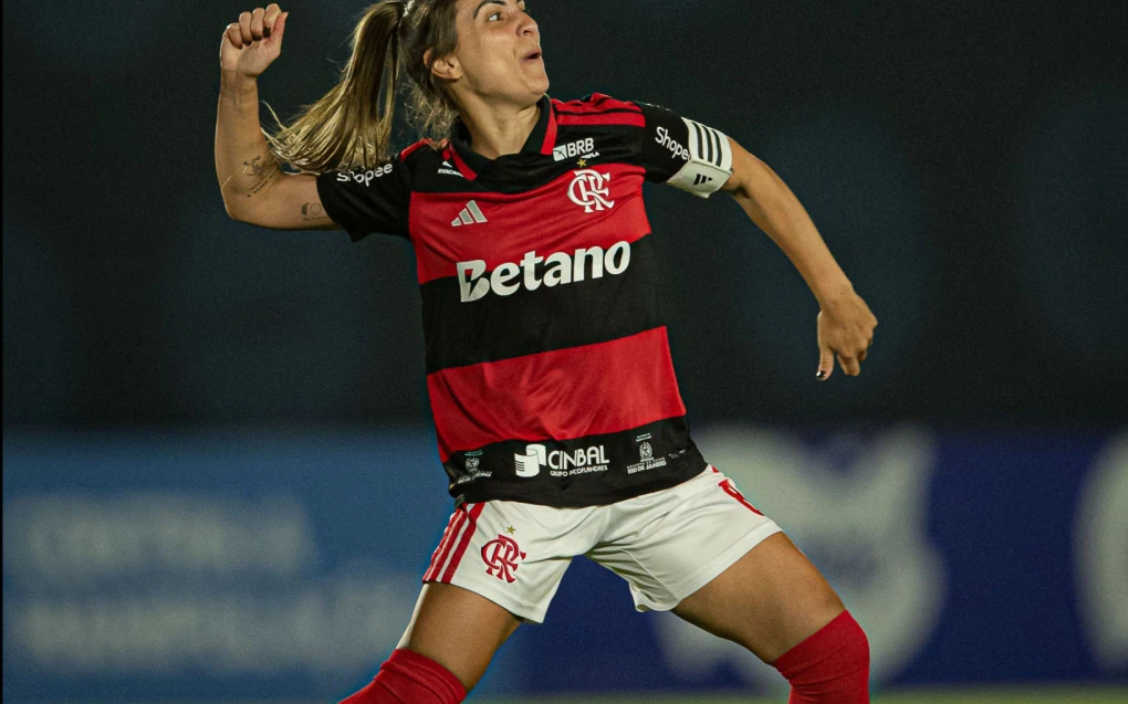 Jogadora do Flamengo comemorando com os braços erguidos e torcida ao fundo