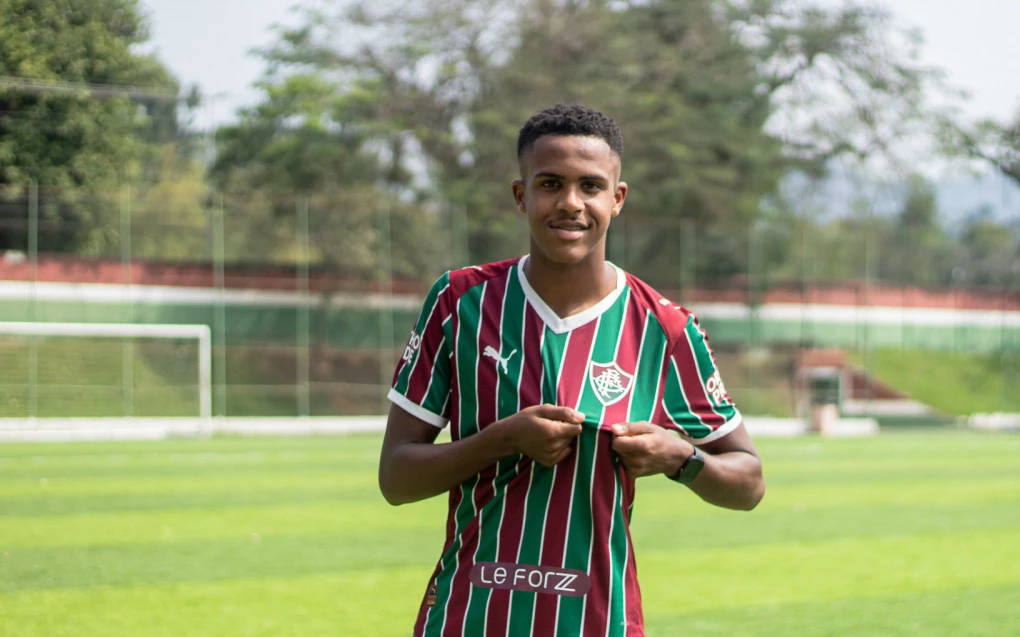 Isaque posando com a camisa do Fluminense, sorrindo e segurando a camisa do clube