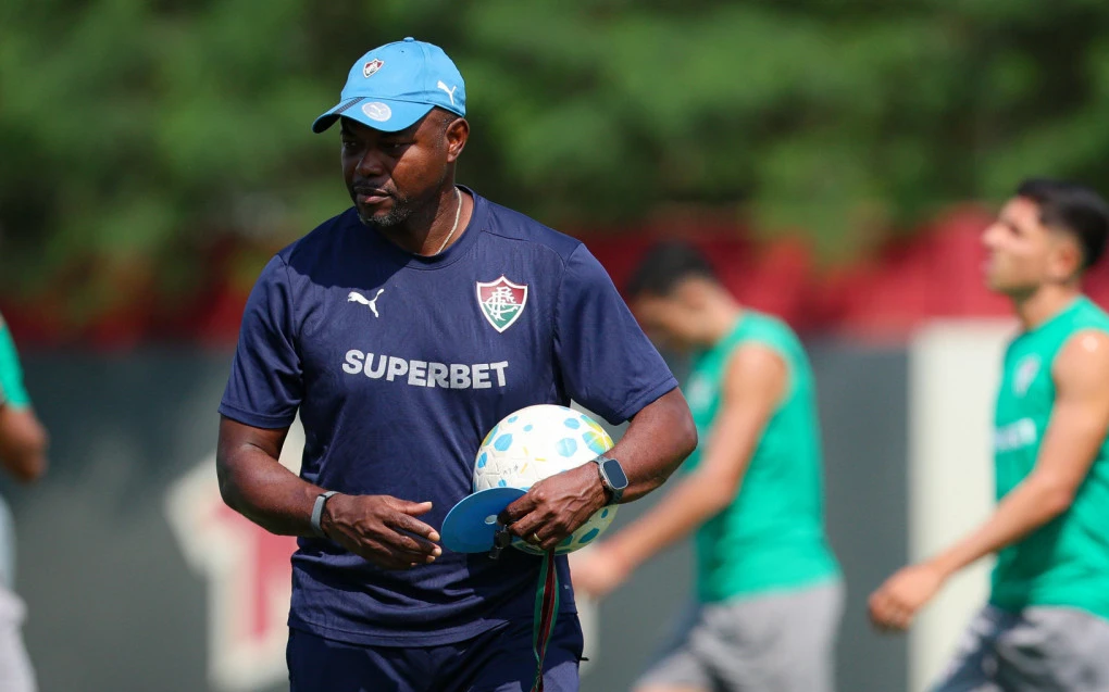 Técnico Marcão comandando treino do Fluminense no centro de treinamento, jogadores ao fundo